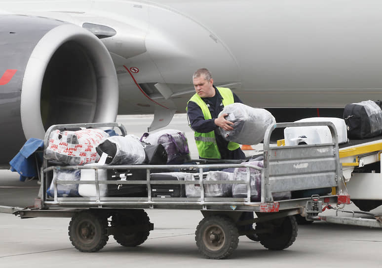 Работник аэродромной службы разгружает багаж самолета в тележку