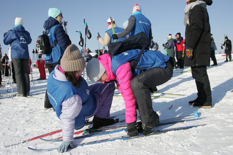 Участники корпоративного забега помогают друг другу надеть лыжи