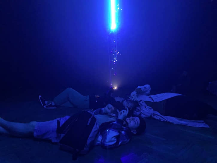Зрители лежат на полу и смотрят лазерную инсталляцию в DKRT