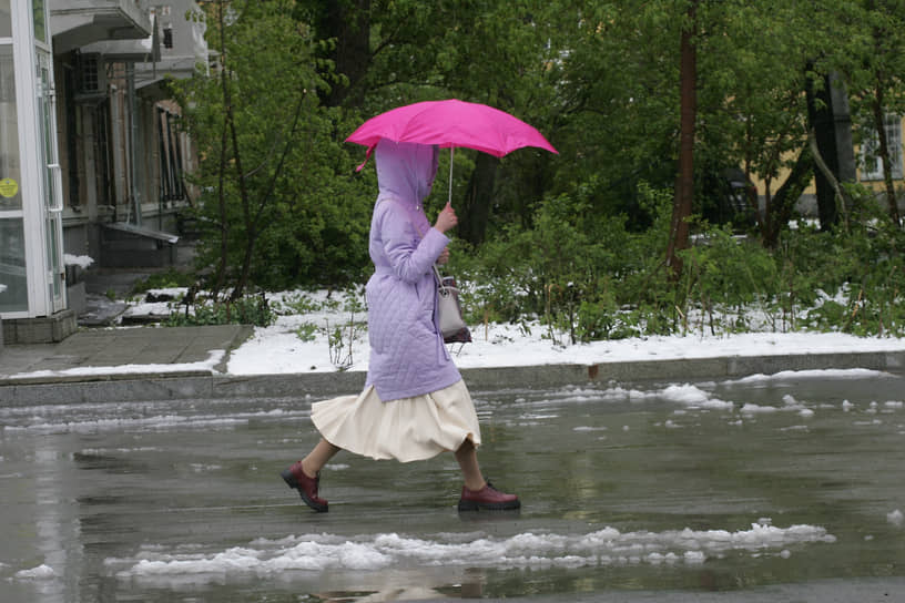 Последствия ночного снегопада на городских улицах. Женщина идет по тротуару под зонтом