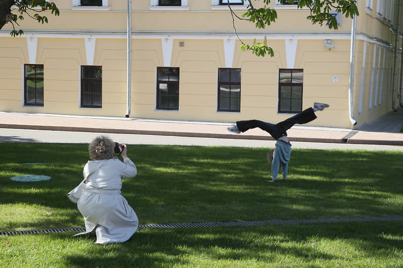 Женщина фотографирует дочь, стоящую на руках в кремлевском сквере