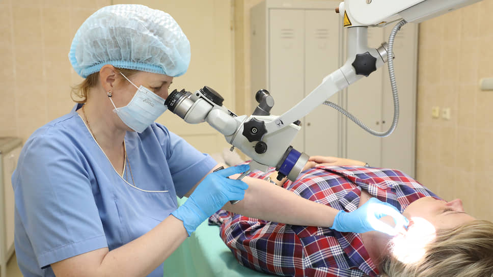 Смотровои ЛОР-кабинет. Врач осматривает ухо пациента с помощью микроскопа