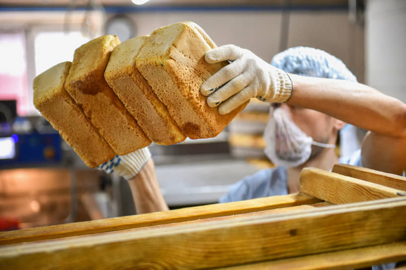 Работа хлебного комбината &quot;Хлебообъединения &quot;Восход&quot; в Новосибирске. Работник загружает булки белого хлеба в аппарат для нарезки
