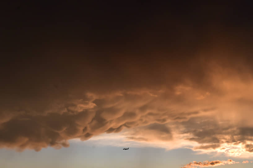 Самолет летит во время закатного предгрозового неба на фоне облаков редкого типа — &quot;вымеобразные облака&quot; (Mammatus clouds)