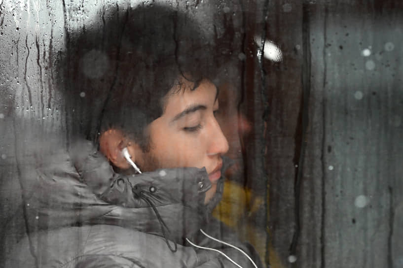 Молодой человек в наушниках за стеклом автобуса во время снегопада в Омске