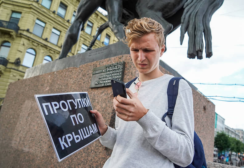 Молодой человек на Аничковом мосту с рекламной табличкой экскурсий «Прогулки по крышам»