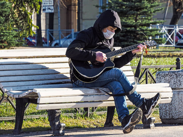 Мужчина в медицинской маске играет на гитаре в сквере города Колпино