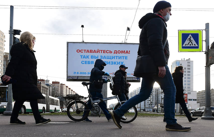 Пешеходы идут под билбордом с социальной рекламой: &quot;Оставайтесь дома! Так вы защитите себя и близких.&quot;