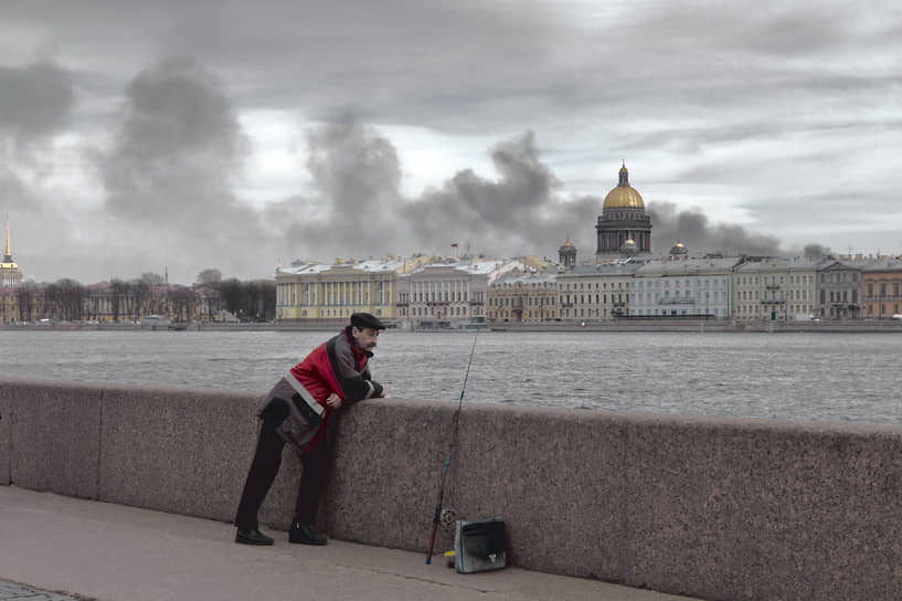 Мужчина ловит рыбу на фоне дыма от пожара в зданиях компании &quot;Невская мануфактура&quot;