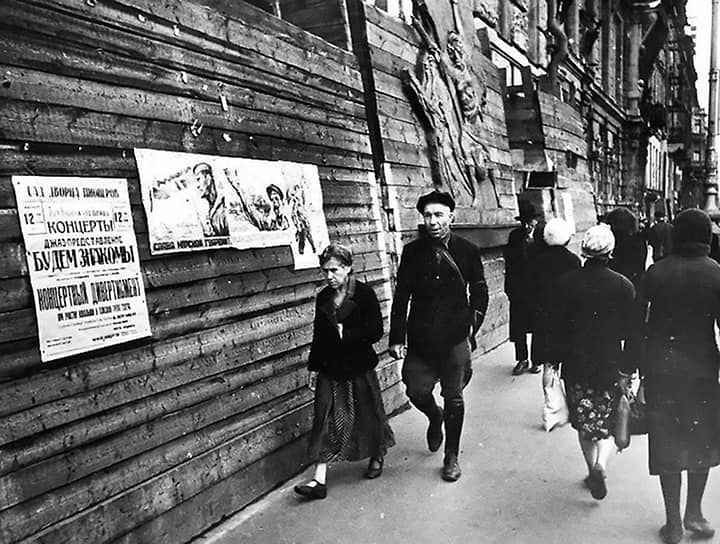 Июль 1942 г. Горожане идут по улице на фоне патриотических плакатов и афиши концертов во Дворце пионеров