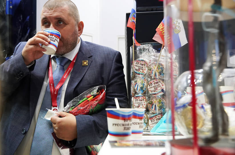 Участник форума пьет кофе на стенде Луганской народной республики (ЛНР) из бумажного стаканчика с надписью: «10 лет русской весне»