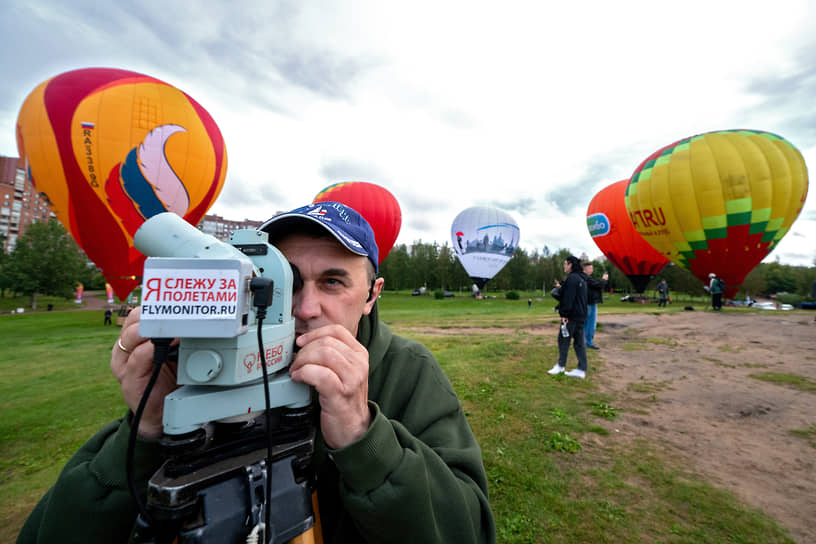 Участник полетов смотрит в оптический нивелир с надписью «Я слежу за полетами» на фоне воздушных шаров