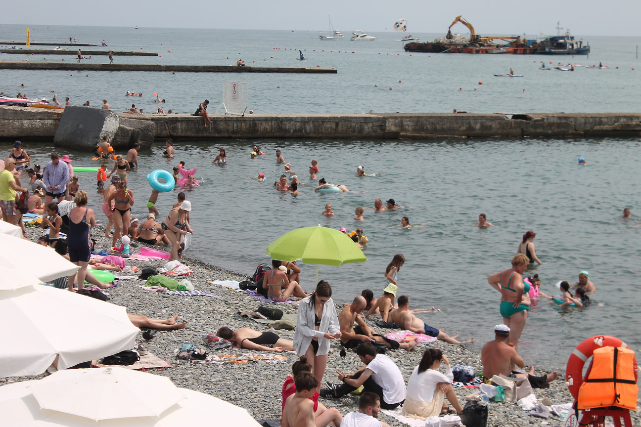 Туристы прячутся под зонтами на пляже и плещутся в море