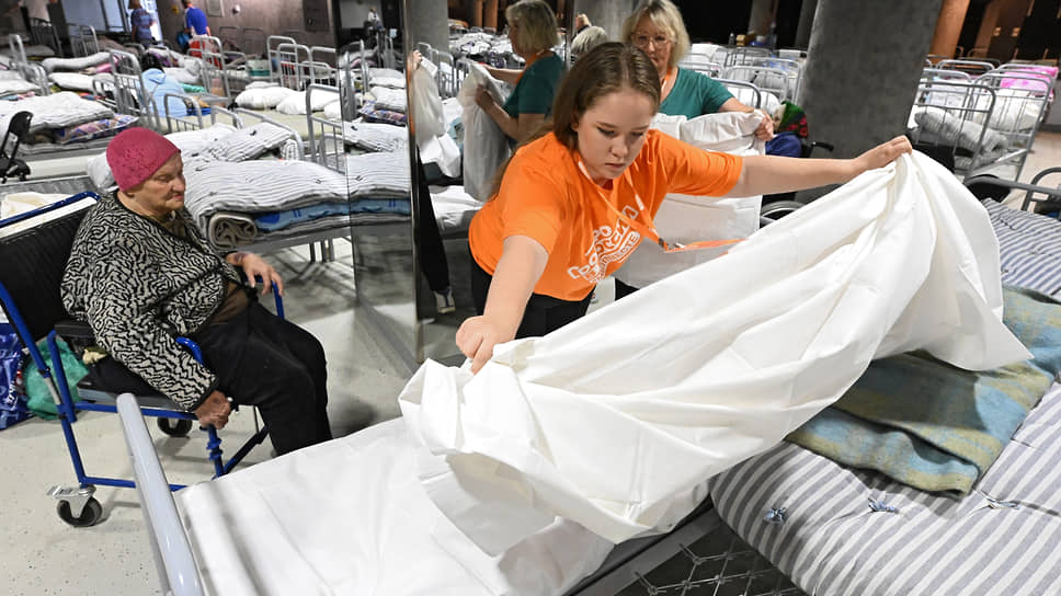 Волонтеры в оранжевых майках раскатывают матрасы и застилают постельное белье 