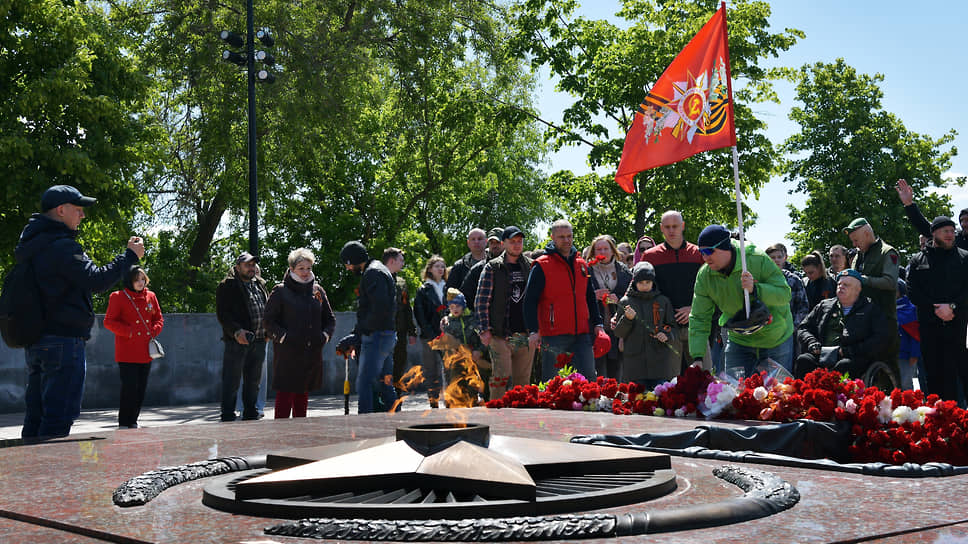Люди возлагают цветы у вечного огня на площади Победы