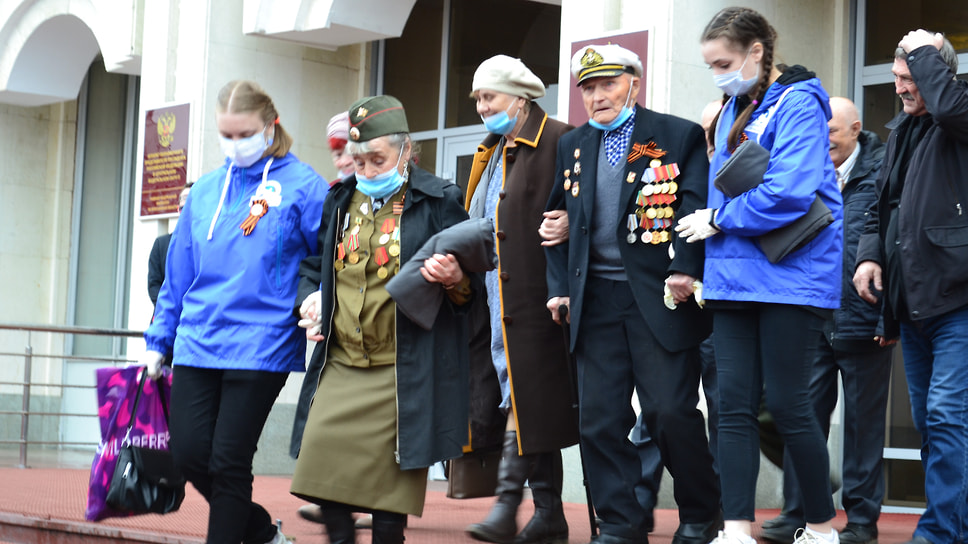 Волонтеры помогают ветеранам Великой Отечественной войны спуститься с лестницы.